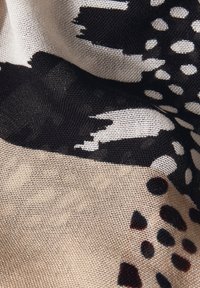 Printet stof med sorte abstrakte former og prikker på en beige baggrund. Teksturen virker glat og vævet med synlige fibre.