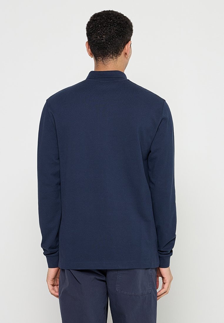 Navyblaues Langarm-Polohemd mit Kragen, weicher Textur und geradem Saum. Von hinten dargestellt, ohne sichtbare Muster oder Akzente.