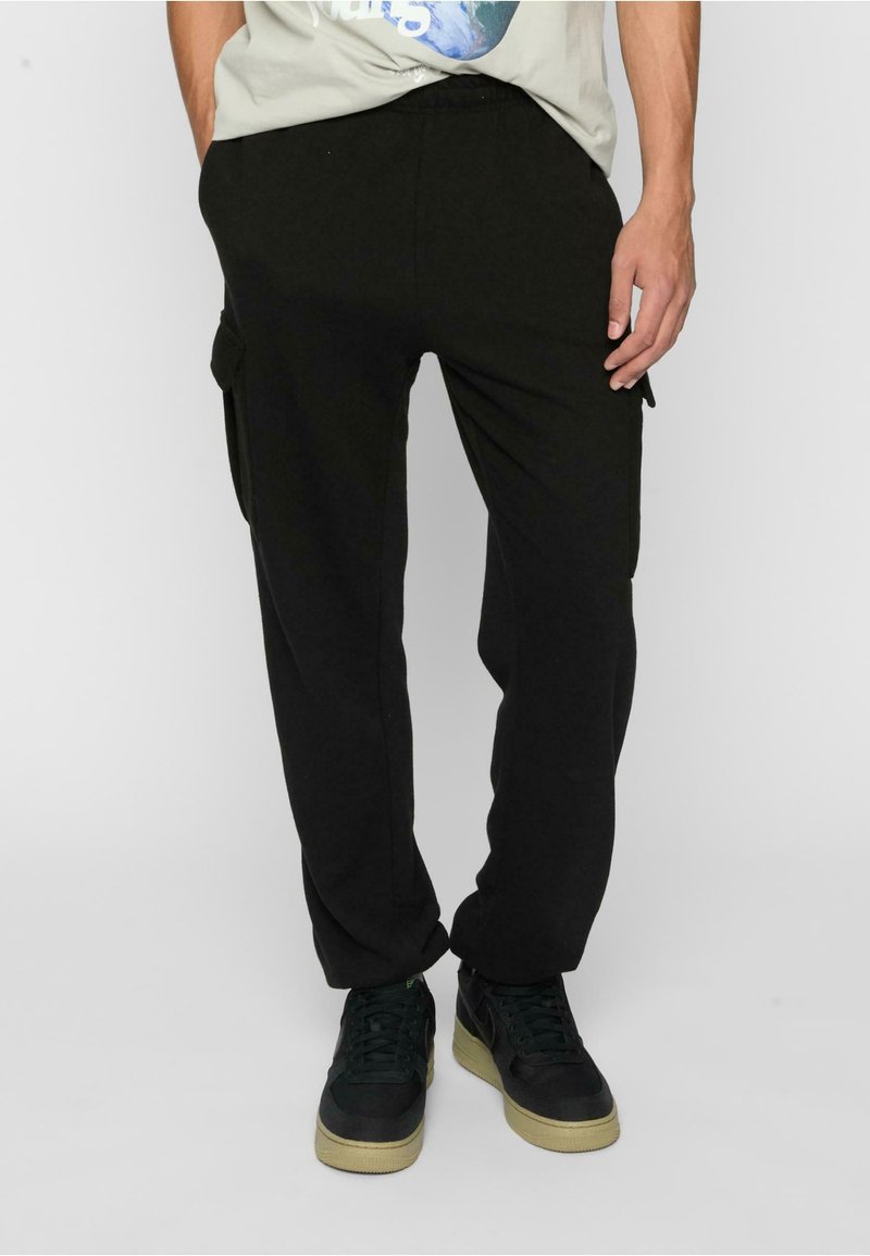 Black cargo pants with an elastic waistband, featuring side pockets. Worn with a light gray graphic t-shirt and dark sneakers.