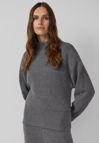 Pull gris en maille avec un col montant côtelé, des épaules tombantes et une coupe décontractée. Présente un tissu texturé et des détails en bord-côte à l'ourlet.