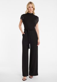 Zwarte jumpsuit met korte, met pailletten bedekte mouwen, een hoge halslijn, brede benen en een strikkoord in de taille. Glad materiaal met een elegante afwerking.
