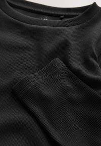 Top negro de manga larga con costillas, con un escote redondeado y tejido texturizado. Presenta costuras visibles y una vista de cerca del detalle de la manga.