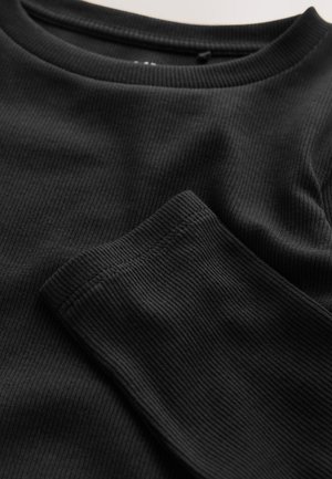 Top negro de manga larga con costillas, con un escote redondeado y tejido texturizado. Presenta costuras visibles y una vista de cerca del detalle de la manga.