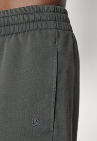 Pantalones de chándal gris oscuro, hechos de una tela suave, con una cinturilla elástica, bolsillos laterales y un pequeño logo bordado en el muslo izquierdo.
