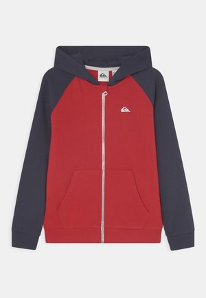 Sweatshirt à capuche rouge et marine avec une fermeture éclair avant, des poches kangourou et un petit logo sur la poitrine. Fabriqué en tissu doux et respirant.
