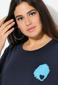 Marinblå t-shirt med rund halsringning, med en ljusblå hjärt-design på bröstet. Mjuk tyg, avslappnad passform och korta ärmar.