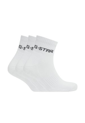 Trois paires de chaussettes blanches à la cheville avec des bordures côtelées et le texte noir G-STAR sur le bord supérieur, présentées empilées côte à côte.