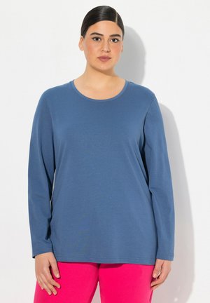 Langärmeliges Oberteil aus festem blauen Baumwollstoff mit rundem Ausschnitt. Weiche Textur und lockere Passform. Kombiniert mit knalligen rosa Hosen.