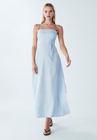 Vaaleansininen maxi-mekko, jossa on neliskulmainen pääntie, säädettävät olkaimet, solmittava vyötäröyksityiskohta ja progressiivinen helma nilkkapituuteen.