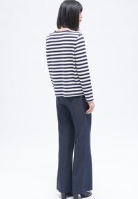 Marineblauwe en witte gestreepte blouse met lange mouwen, gecombineerd met donkere flared broeken. De blouse heeft een ronde halslijn en een rechte snit.