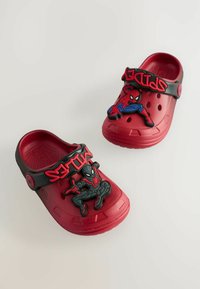 Zoccoli rossi modellati con una tracolla nera che presenta accenti 3D di Spider-Man e Miles Morales. Suola testurizzata con fori di ventilazione, materiale in gomma.