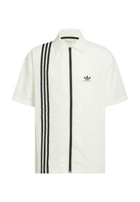 Camicia a maniche corte di colore crema con chiusura a zip nera e tre strisce nere verticali sul lato sinistro. Presenta un piccolo logo.