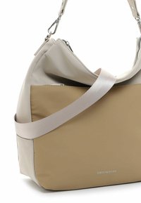 Bolso hobos con una parte superior gris claro, base beige, material texturizado, herrajes plateados, y una amplia correa plana para el hombro. Logo grabado en el costado.