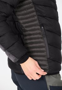 Sort pufferjakke med en glat sidepanel med ribbet tekstur, lynlåslomme og elastiske manchetter for en tætsiddende design.