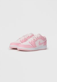 Rózsaszín és fehér Nike sneaker, sima bőr felső résszel, perforált lábujjrésszel, kerek fűzőkkel és texturált tapadású gumitalppal.