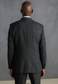 Sacou de culoare gri cărbune, cu un țesut texturat. Are un slit singular și manșete cu nasturi. Vederea din spate dezvăluie un design ajustat.