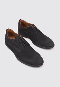 Chaussures en daim noir avec un bout arrondi, des accents en cuir marron contrastant et des lacets noirs. Semelle en caoutchouc pour une meilleure adhérence et durabilité.