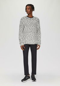Grauer undweißer gestrickter Pullover mit langen Ärmeln, dunkle Denim-Hosen und schwarze Sneakers. Das Outfit weist ein strukturiertes Muster auf.