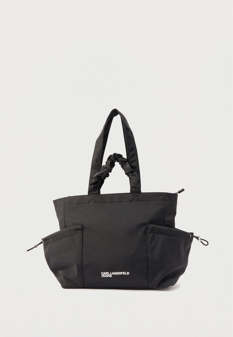 Μαύρη τσάντα ώμου με δύο επενδεδυμένες λαβές, δύο πλαϊνές τσέπες με φερμουάρ και λευκό λογότυπο "Karl Lagerfeld Jeans" στο κέντρο μπροστά.