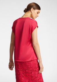 Top in raso rosso con maniche corte, texture liscia, scollatura rotonda, abbinato a una gonna in pizzo rosso con motivi floreali e bordi a onda.