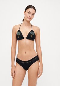 Bikini di crochet nero con reggiseno triangolare decorato da ricami di palme e slip coordinato con bordi a increspature.