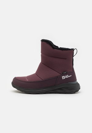 Botte d'hiver mi-hauteur de couleur marron rouge avec doublure en fourrure noire, semelle épaisse noire, languette de traction au talon, et logo Jack Wolfskin sur le côté du talon.
