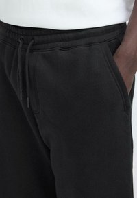 Schwarze Jogginghose aus weichem Stoff, mit einem elastischen Taillenbund und Kordelzug sowie seitlichen Taschen. Die glatte Textur verbessert den Tragekomfort.