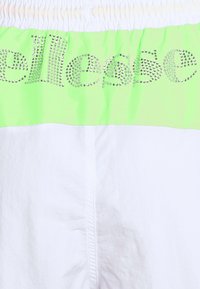 Vita shorts med en samlad midja, accentuerade av en ljusgrön panel med rhinestoneskrifter, vilket skapar en glänsande, iögonfallande detalj.