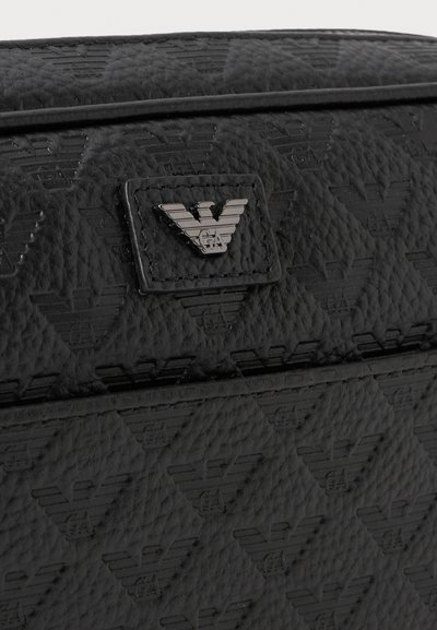 Suprafață de piele neagră, embossată cu un model repetat de logo cu vultur și un mic patch metalic cu un emblema de vultur în centru.