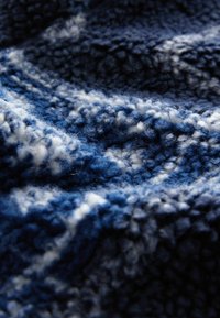 Blauwe en witte pluche stof met een gestructureerd, fluffy oppervlak, met een golvend patroon door de stof heen.