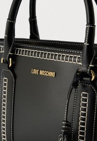 Μαύρη δερμάτινη τσάντα χειρός με λευκή ραφή. Διαθέτει χρυσό λογότυπο «LOVE MOSCHINO» και διαμορφωμένο σχήμα. Ανθεκτικές χειρολαβές με διακοσμητικά στοιχεία.
