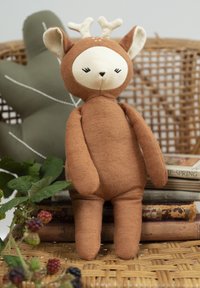 Mäkká plyšová hračka hnedej farby s krémovými detailmi, jeleňové uši a parožie. Má vyšívané detaily na tvári. Na pozadí je tkaná textúra s rastlinami.