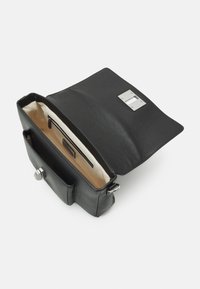 Black leather bag with a textured finish, top flap, and silver hardware. Interior features a beige lining and a zippered pocket for storage.