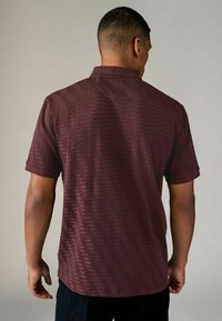 Camisa de manga corta en burdeos con un patrón de espiga texturizado. Diseño con cuello y mangas enrolladas, hecha de un tejido suave.