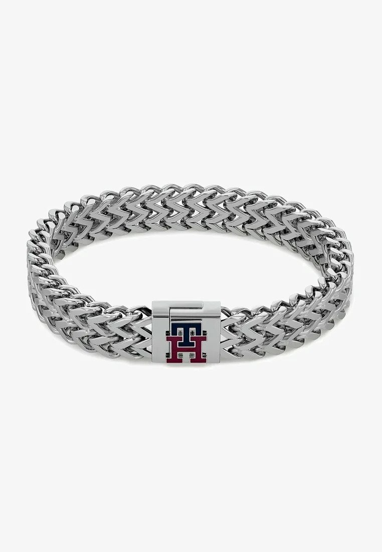 Metallarmbånd med en flettet design i sølv og en rektangulær lås, prydet med en logo i blå og røde farger.