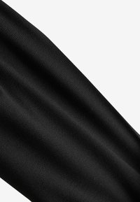 Gros plan sur un tissu noir lisse avec un tissage finement texturé et des plis doux sur un fond blanc.