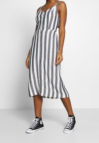 Pruhované midi šaty v námořnické modré a bílé, s tenkými ramínky a knoflíkovým zapínáním vpředu. Kombinováno s černými vysokými teniskami.