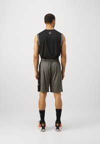 Camiseta deportiva sin mangas negra y pantalones cortos grises, ambos fabricados con tejido ligero. Los pantalones cortos cuentan con una cinturilla elástica y acentos de logo.
