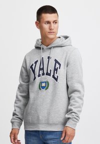 Šedá mikina s kapucňou a šnúrkami, so slovom "YALE" v námorníckej modrej farbe a dizajnom odznaku so vavrínovým vzorom v strede.