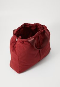 Borsa a spalla rossa in tessuto con una superficie morbida e texture, caratterizzata da un'apertura arricciata e due manici robusti. L'interno è ampio e non foderato.