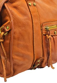 Sac à main en cuir marron avec des coutures contrastées, une poche zippée et des accents en laiton. Surface douce et texturée avec une forme arrondie.