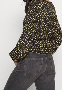 Czarna bluzka w żółty kwiatowy wzór, z długimi rękawami i marszczonym pasem, połączona z ciemnoszarymi dżinsami z tylnymi kieszeniami i prostym krojem.