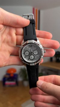 Montre argentée avec un cadran gris texturé, trois sous-cadrans, lunette octogonale ornée de cristaux, bracelet en caoutchouc noir, boucle en acier inoxydable.