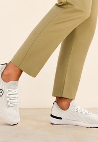 Weiße Sportschuhe aus strukturiertem Strickmaterial mit schwarzen Akzenten an der Ferse, getragen mit khakifarbenen, cropped Hosen.