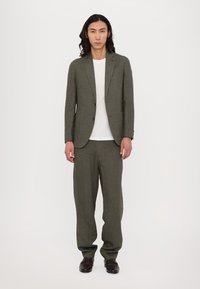 Olive green linen suit with a fitted blazer and loose trousers, paired with a white t-shirt. Smooth texture and tailored design.