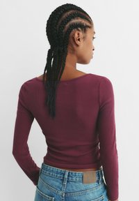 Top a maniche lunghe in maglia a coste color bordeaux, con scollatura ampia e forma aderente, abbinato a jeans in denim blu a vita alta.