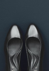 Scarpe nere in pelle con tacco alto, punta affusolata, texture liscia e dettagli a taglio sui lati. Design semplice su uno sfondo scuro.