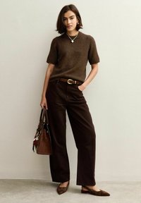 Pull en tricot marron à manches courtes, large pantalon marron, ceinture dorée, chaussures plates marron et sac à main marron avec des accents. Look décontracté et cohérent.