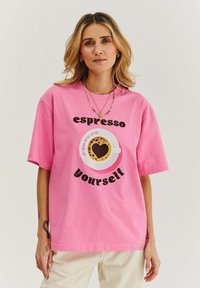 Růžové bavlněné tričko s grafickým potiskem šálku kávy s latte art ve tvaru srdce a textem "espresso yourself" v tučném černém písmu.