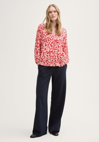 Blusa a maniche lunghe con motivo rosso e rosa e scollo a V, abbinata a pantaloni larghi blu navy e scarpe nere. Tessuto dalla texture liscia.
